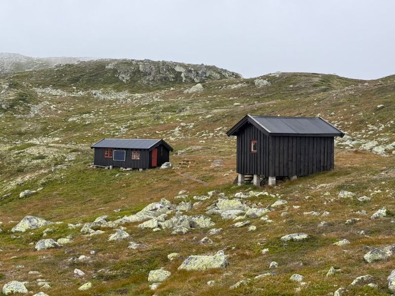 Såtehytta og uthuset på den grønne fjellryggen en dag med lavt skydekke