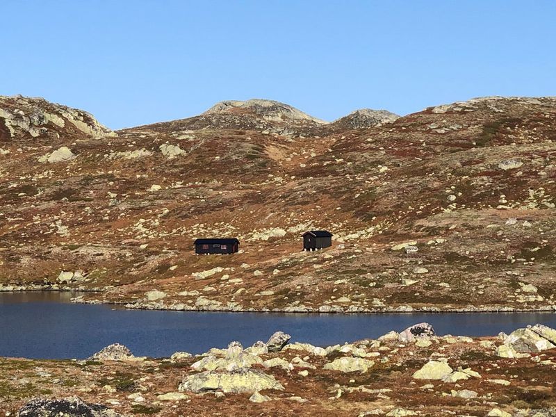 Såtehytta og uthuset sett over Såtetjønn, som to små mørke hus på den brune fjellryggen