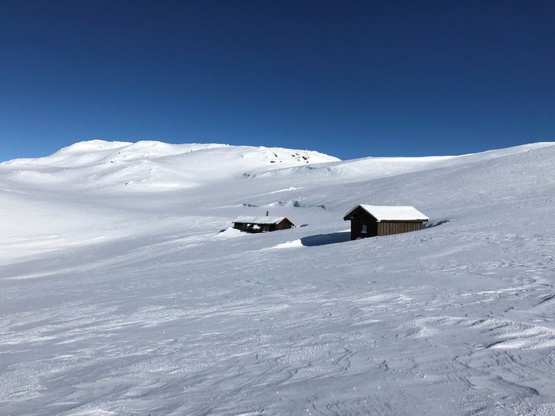 Såtehytta nedsnødd om vinteren, som en mørk strek i et hvitt fjellandskap