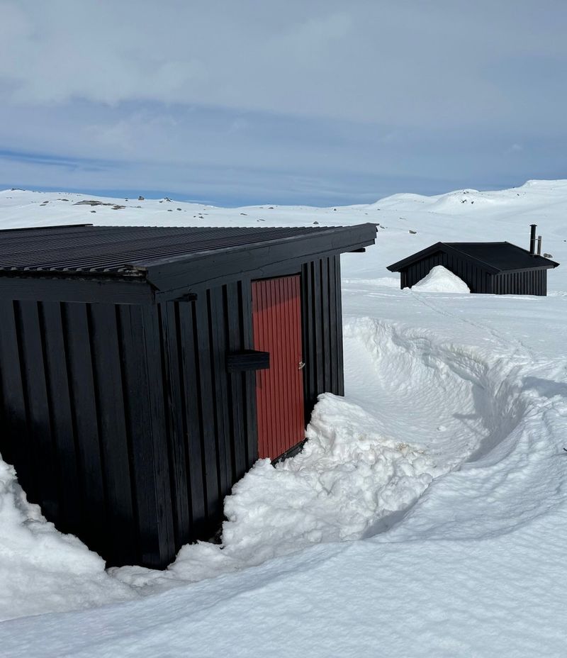 Trollheimen om vinteren med rød dør og oppmåkt snøgang inn til hytta, uthuset bak